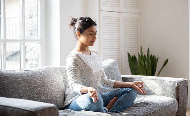 Meditation: Frau meditiert auf der Couch